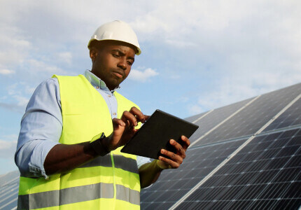 engineer looking at a tablet with a solar panel behind him
