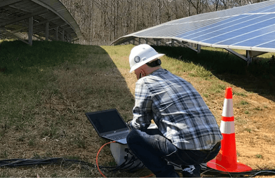 man in hardhat looking at laptop near solar panels