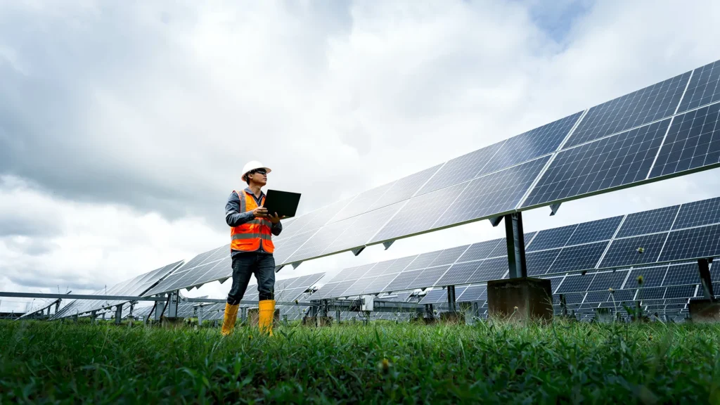 Field worker checking laptop next to solar panels